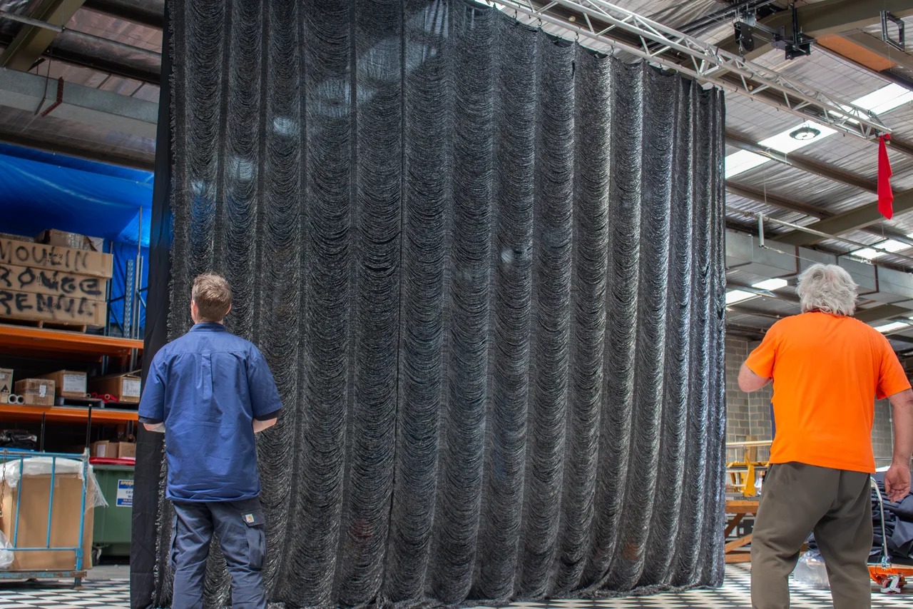 Two workers inspecting a black tinsel drape for Moulin Rouge hung from a workshop track