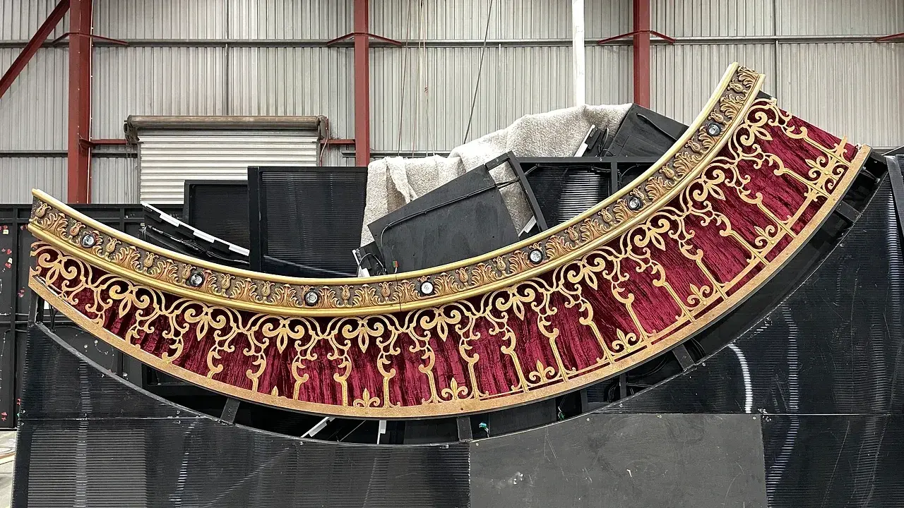 A Moulin Rouge heart portal arc in the TSA scenic workshop - red velvet and gold filigree face with lamp fittings along the moulding and the frame behind. Photo: TSA.