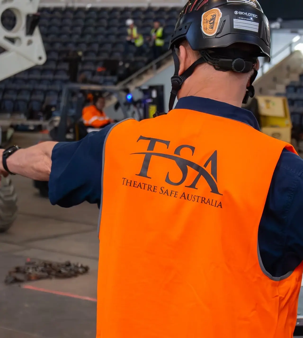 A TSA rigger in hi-vis directing a rigging crew on an arena install